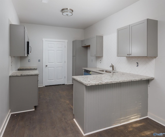 kitchen with tasteful backsplash, a peninsula, light stone countertops, gray cabinetry, and a sink