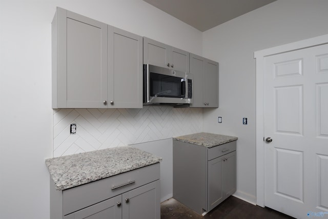 kitchen featuring tasteful backsplash, stainless steel microwave, light stone counters, and gray cabinetry