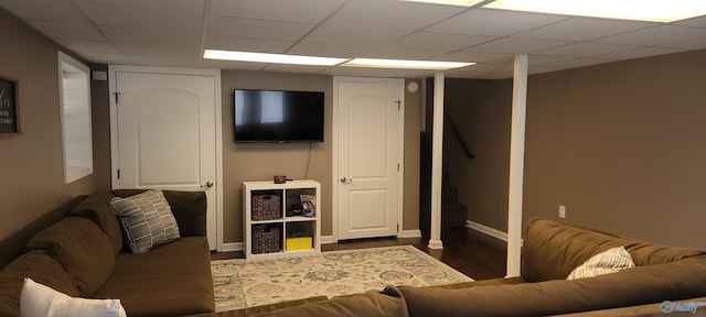 living area featuring dark wood-type flooring, a drop ceiling, and baseboards