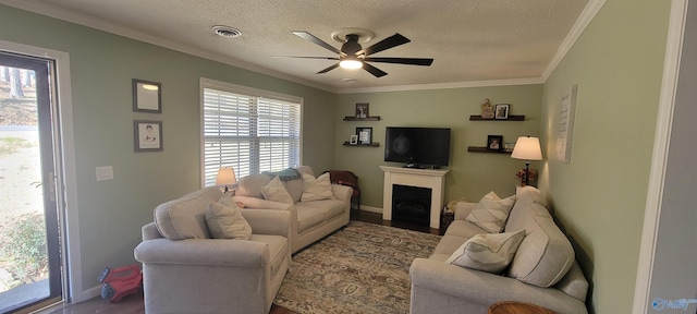 living area with a textured ceiling, a fireplace, visible vents, a ceiling fan, and ornamental molding