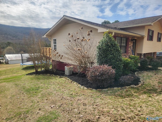 view of side of home featuring a yard, a trampoline, central AC unit, and brick siding