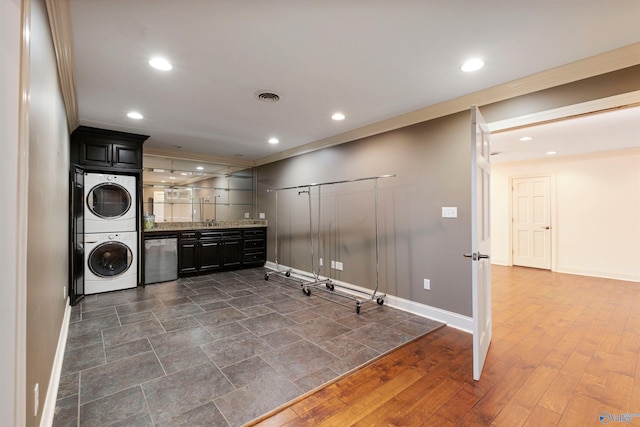 clothes washing area with stacked washer and clothes dryer, dark hardwood / wood-style flooring, crown molding, and sink