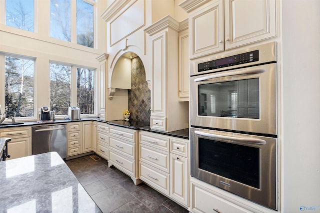 kitchen featuring dark stone counters, cream cabinetry, stainless steel appliances, dark tile patterned flooring, and sink