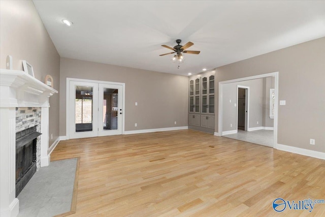 unfurnished living room with a stone fireplace, light hardwood / wood-style flooring, french doors, and ceiling fan