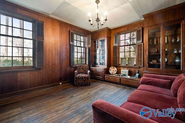 living area with dark hardwood / wood-style floors, ornamental molding, wooden walls, and an inviting chandelier