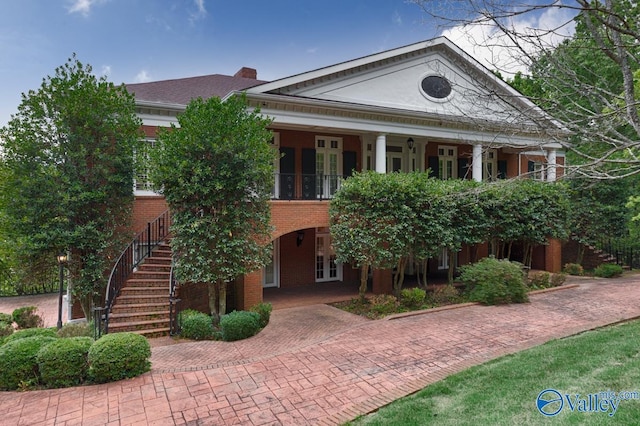 neoclassical / greek revival house featuring a chimney, stairway, french doors, and brick siding