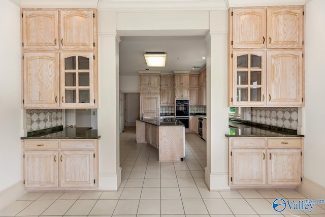 kitchen featuring light tile patterned floors, glass insert cabinets, dark countertops, light brown cabinets, and backsplash