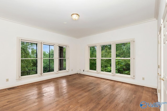 spare room with ornamental molding, visible vents, wood finished floors, and baseboards