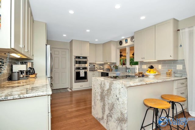 kitchen with light hardwood / wood-style flooring, stainless steel appliances, backsplash, light stone countertops, and a kitchen breakfast bar