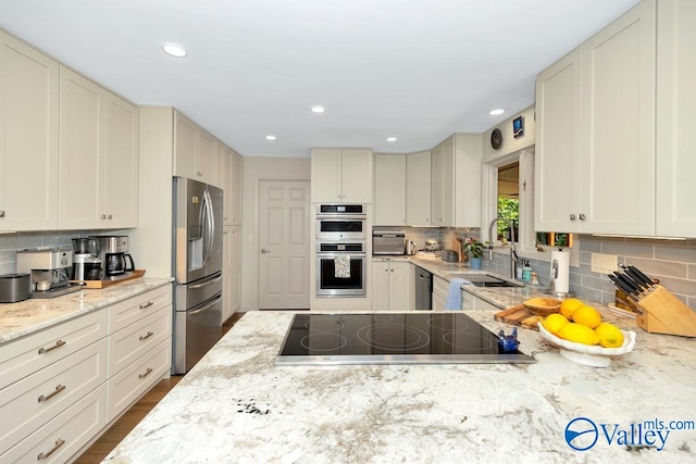 kitchen featuring hardwood / wood-style flooring, tasteful backsplash, stainless steel appliances, sink, and light stone countertops