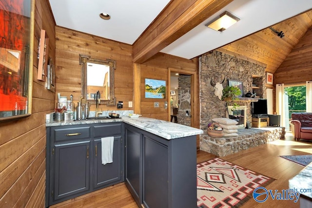 kitchen featuring gray cabinets, wooden walls, light stone counters, lofted ceiling with beams, and light hardwood / wood-style floors