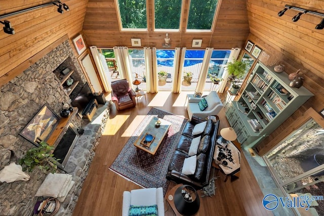 living room featuring wooden walls, hardwood / wood-style floors, rail lighting, and high vaulted ceiling