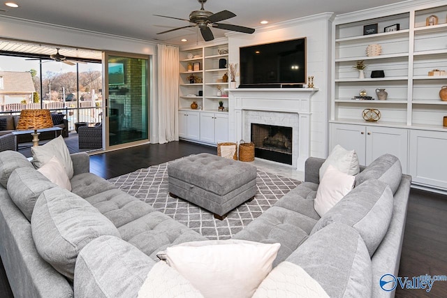 living room featuring dark hardwood / wood-style flooring, built in shelves, ornamental molding, and ceiling fan