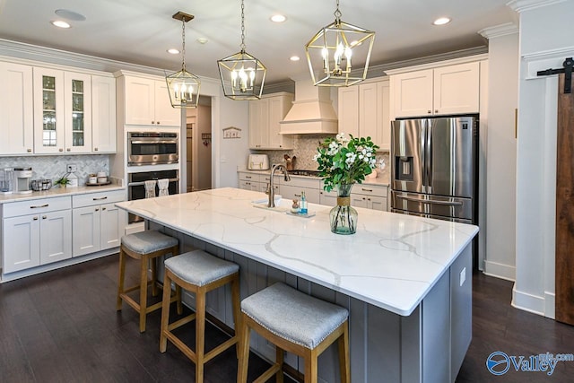 kitchen with stainless steel appliances, custom exhaust hood, a kitchen island with sink, and white cabinets