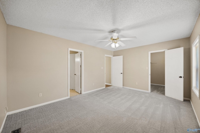 unfurnished bedroom featuring a spacious closet, ceiling fan, a closet, light colored carpet, and a textured ceiling