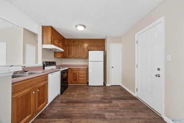 kitchen featuring dark wood-type flooring, sink, white appliances, and a textured ceiling