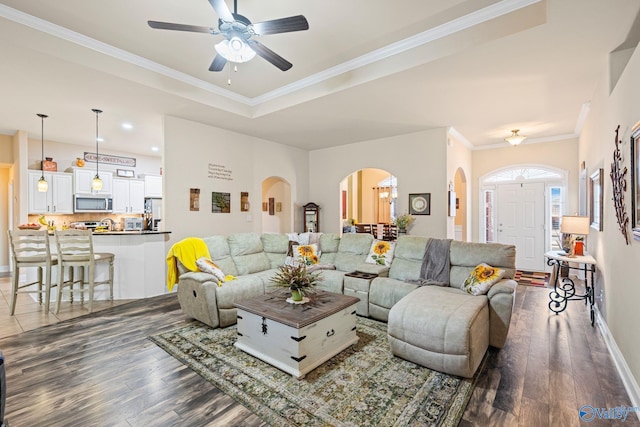 living room featuring crown molding, dark wood-type flooring, a raised ceiling, and ceiling fan