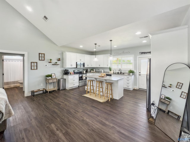 kitchen featuring white cabinets, dark wood-type flooring, appliances with stainless steel finishes, a center island, and a breakfast bar area