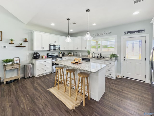 kitchen featuring a kitchen island, dark hardwood / wood-style floors, stainless steel appliances, hanging light fixtures, and white cabinetry