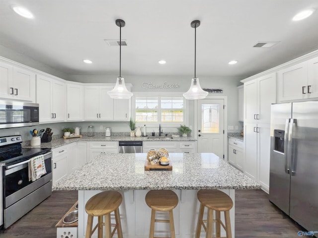 kitchen with hanging light fixtures, a kitchen island, white cabinetry, stainless steel appliances, and dark hardwood / wood-style floors