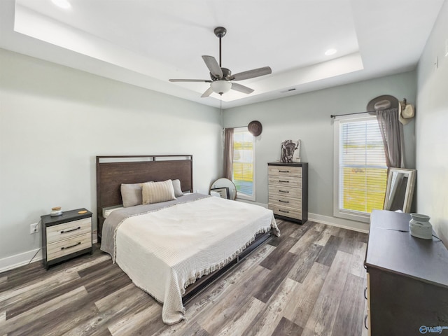 bedroom featuring ceiling fan, a tray ceiling, and dark hardwood / wood-style flooring