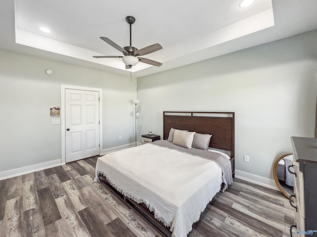 bedroom with ceiling fan, a tray ceiling, and dark hardwood / wood-style floors