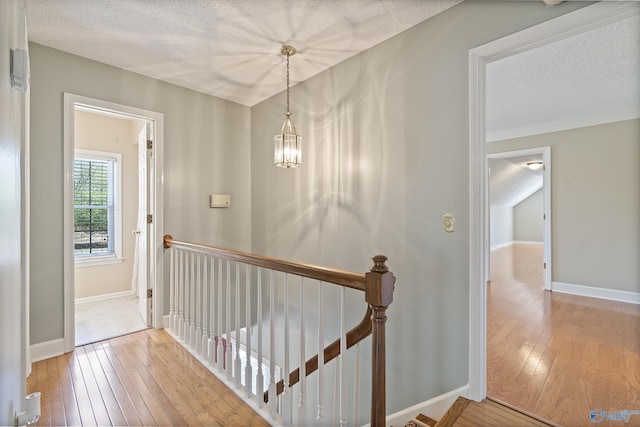 hall with hardwood / wood-style flooring, a chandelier, an upstairs landing, and a textured ceiling