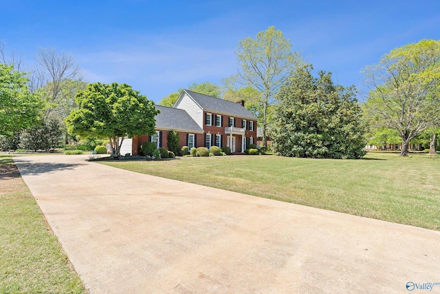colonial home with a front lawn, driveway, brick siding, and a chimney