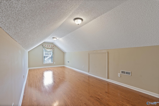 bonus room featuring lofted ceiling, wood finished floors, baseboards, and a textured ceiling