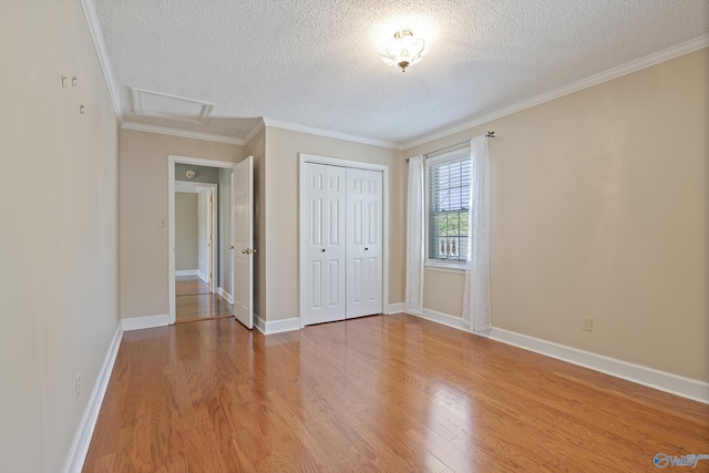 unfurnished bedroom featuring attic access, light wood-style floors, a textured ceiling, and a closet