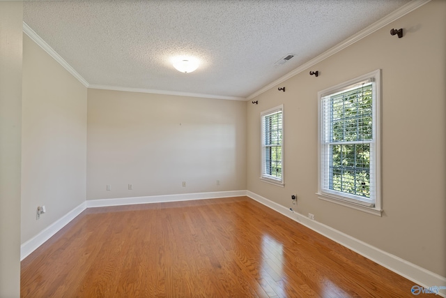 spare room with crown molding, wood finished floors, a textured ceiling, and visible vents