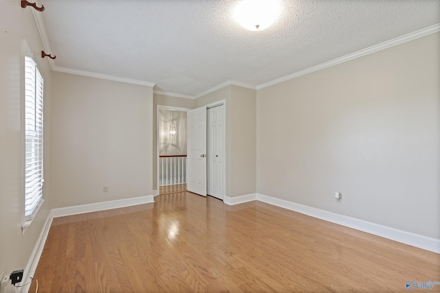unfurnished room featuring light wood-type flooring, a wealth of natural light, crown molding, and baseboards