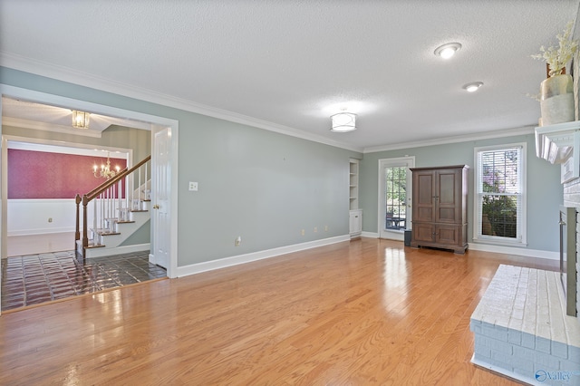 foyer entrance featuring a textured ceiling, light wood-type flooring, a notable chandelier, stairs, and crown molding