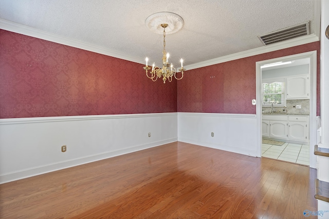 unfurnished room with wood finished floors, a textured ceiling, a chandelier, a wainscoted wall, and visible vents