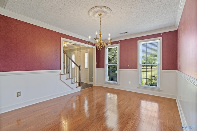 unfurnished dining area with hardwood / wood-style floors, visible vents, a textured ceiling, and a notable chandelier
