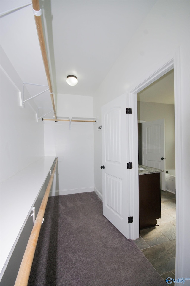 walk in closet featuring beam ceiling and dark colored carpet