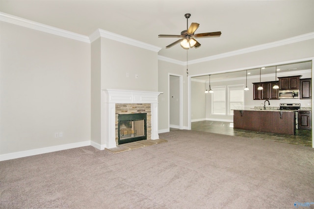 unfurnished living room featuring a tiled fireplace, ceiling fan, carpet flooring, ornamental molding, and sink