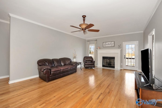 living room featuring ceiling fan, ornamental molding, light hardwood / wood-style floors, and a tile fireplace