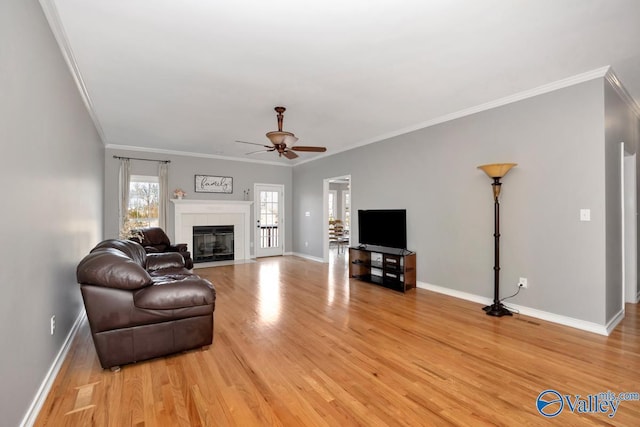 living room with ornamental molding, ceiling fan, a fireplace, and light wood-type flooring