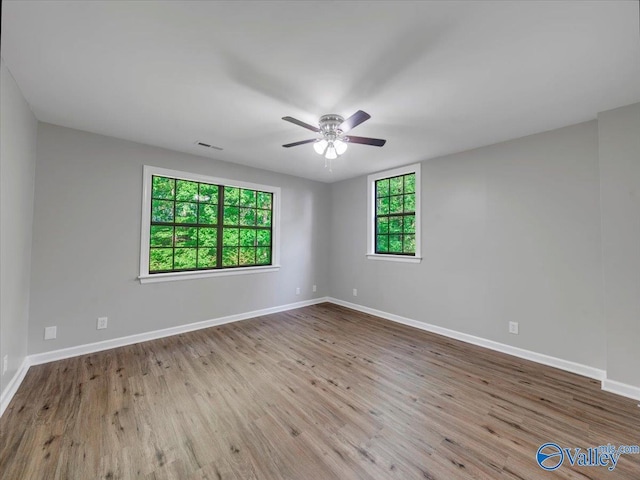 empty room featuring a ceiling fan, baseboards, visible vents, and wood finished floors