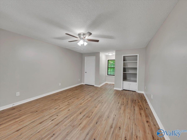 unfurnished room featuring ceiling fan, a textured ceiling, built in features, baseboards, and wood finished floors