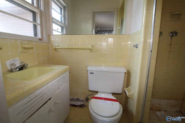 bathroom with tile walls, vanity, toilet, and a tile shower