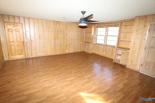empty room with wood-type flooring, wooden walls, and ceiling fan