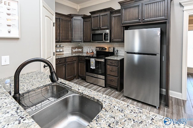 kitchen featuring light stone countertops, appliances with stainless steel finishes, ornamental molding, dark brown cabinets, and sink