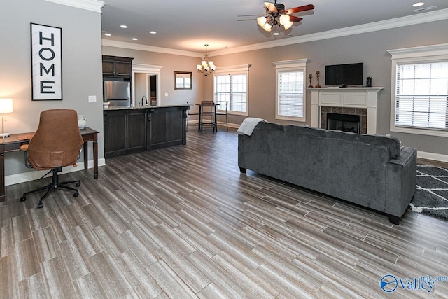 living room featuring a tiled fireplace, crown molding, hardwood / wood-style floors, and ceiling fan with notable chandelier