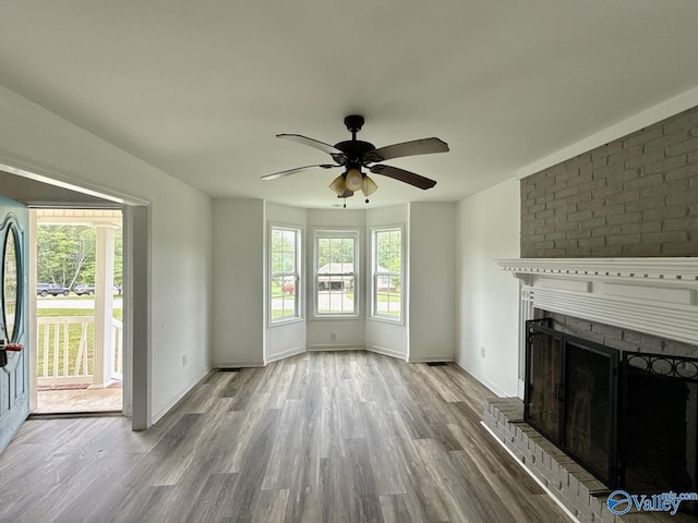 unfurnished living room with wood finished floors, a ceiling fan, a brick fireplace, and baseboards