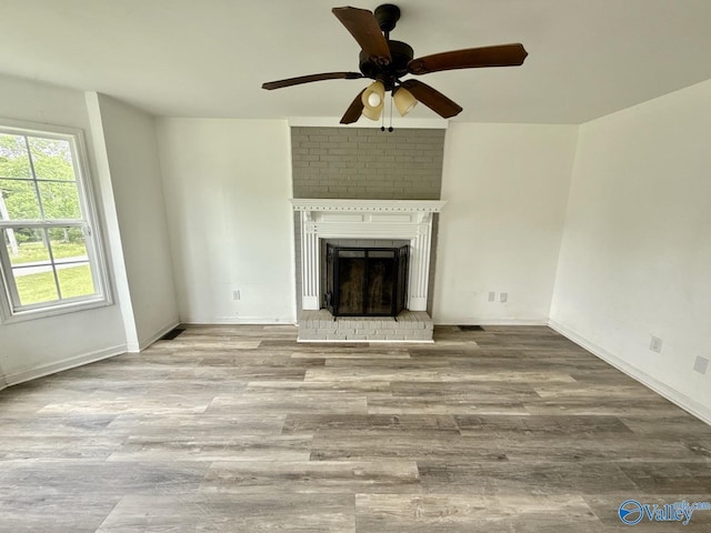 unfurnished living room featuring wood finished floors, a brick fireplace, a ceiling fan, and baseboards