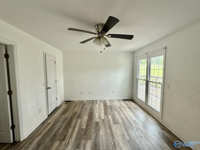 empty room with wood finished floors, a ceiling fan, and baseboards