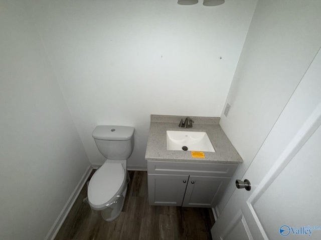 half bathroom with wood finished floors, vanity, toilet, and baseboards