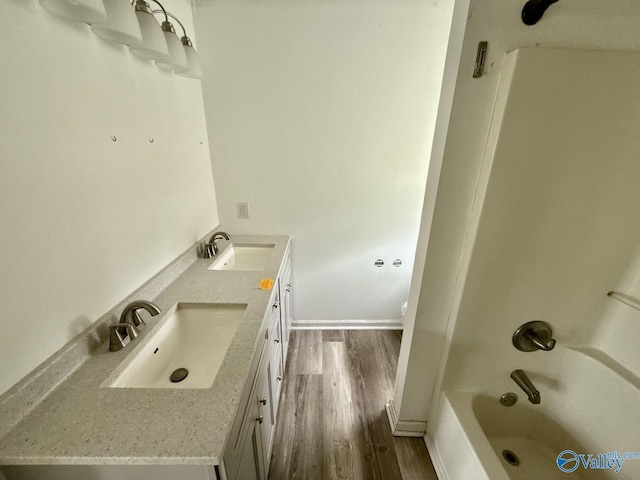 full bathroom featuring wood finished floors, double vanity, shower / washtub combination, and baseboards